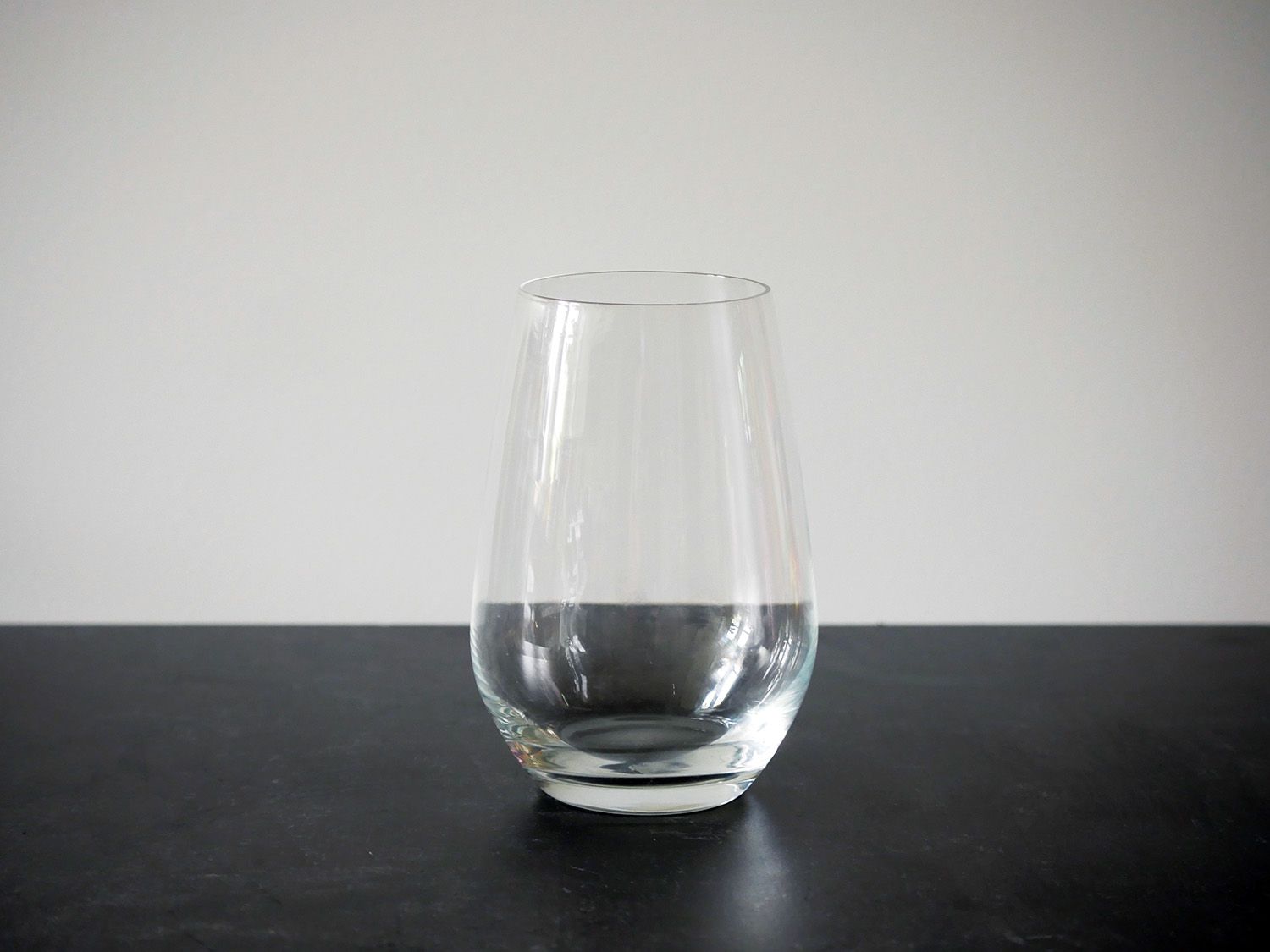 Schott zwiesel stemless wine glass on black countertop with white backdrop