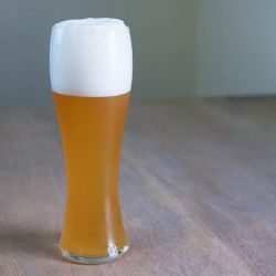 A tall pint glass of a hazy, golden wheat beer.