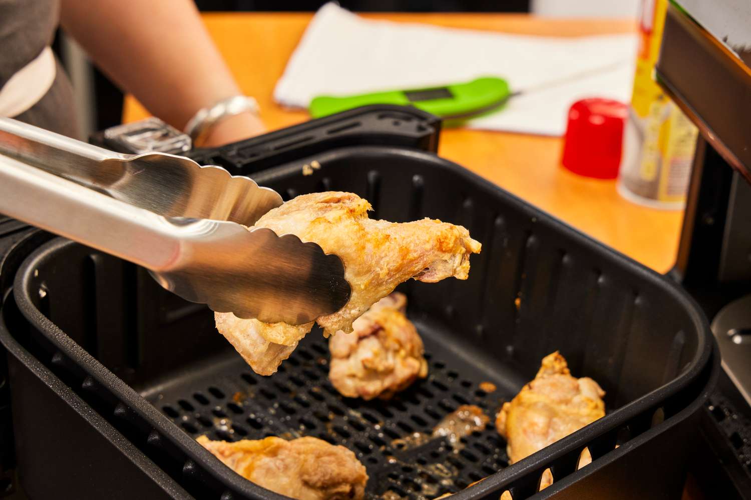 Tongs holding a piece of chicken over the Cosori Pro II 5.8 Quart Air Fryer Oven Combo basket 