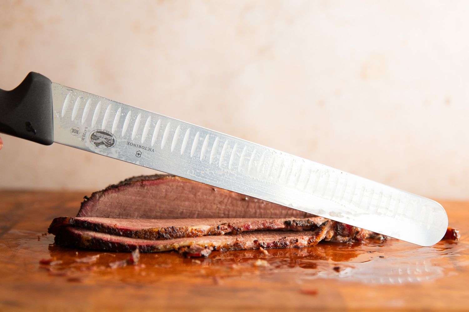 A person slicing meat using the Victorinox Fibrox Pro Slicing Knife