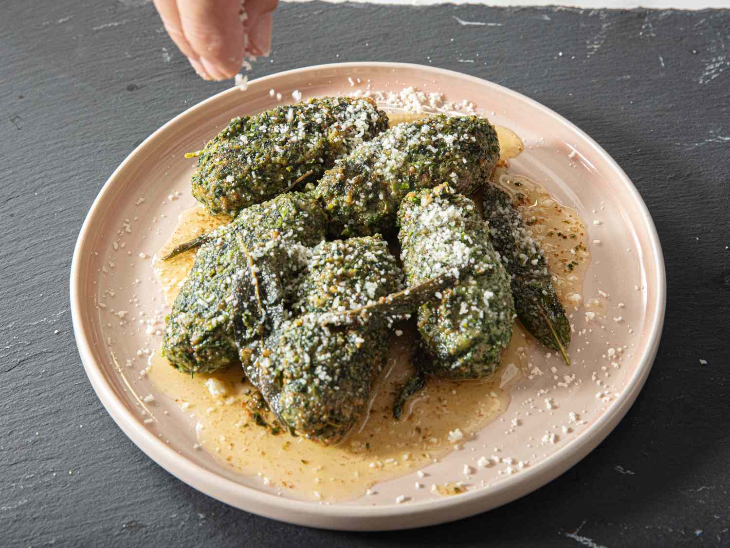A plate of cooked spinach dumplings being sprinkled with grated cheese