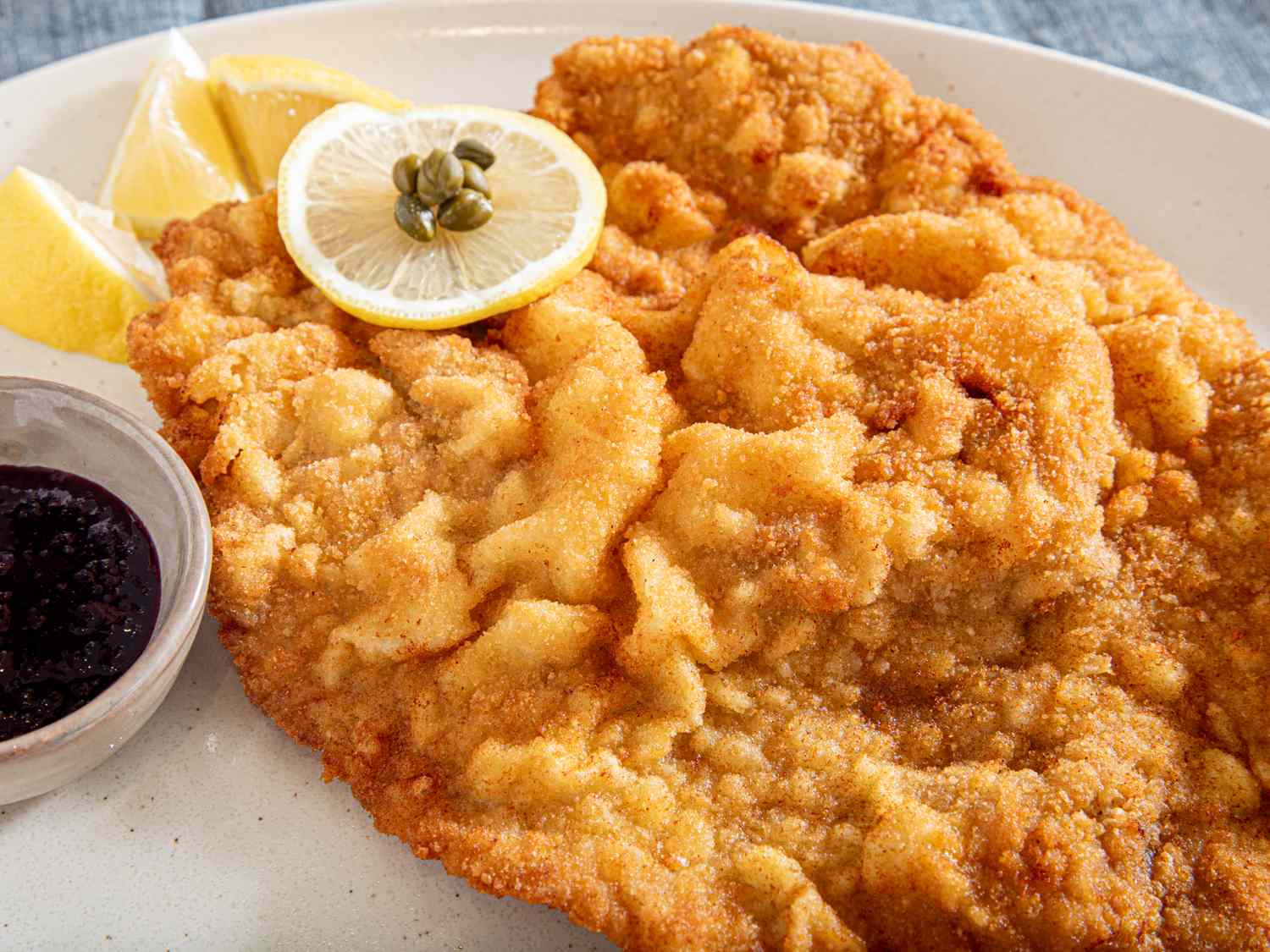Wienerschnitzel on a plate with lemon slices and a side sauce