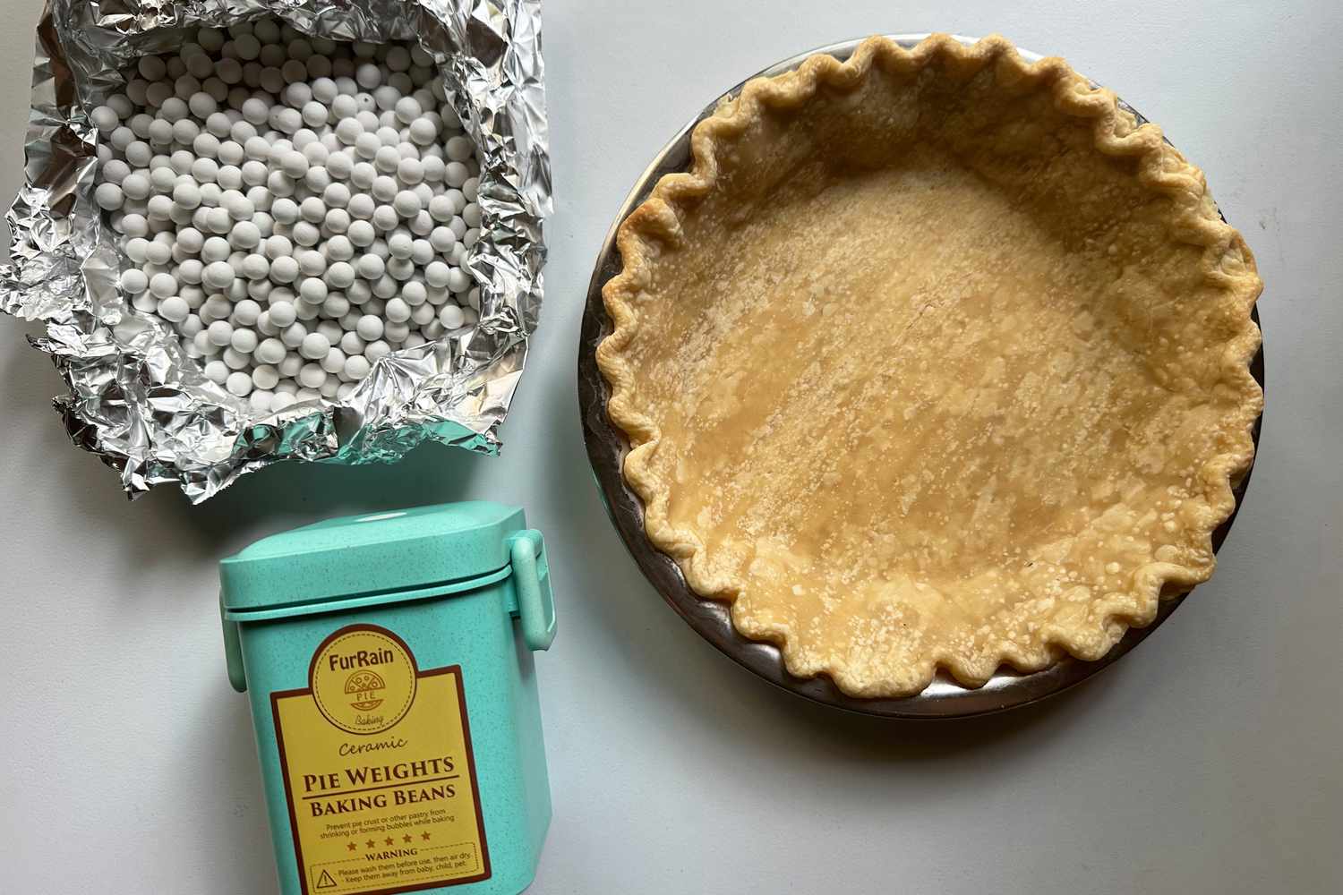 A baked pie shell next to a foil liner full of ceramic pie weights