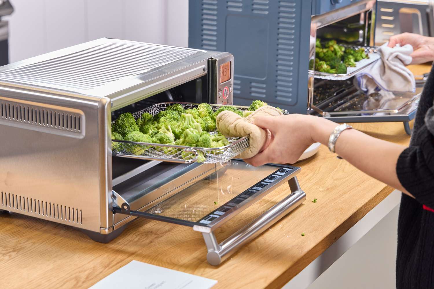 A person places broccoli into the Breville The Smart Oven Air Fryer Compact