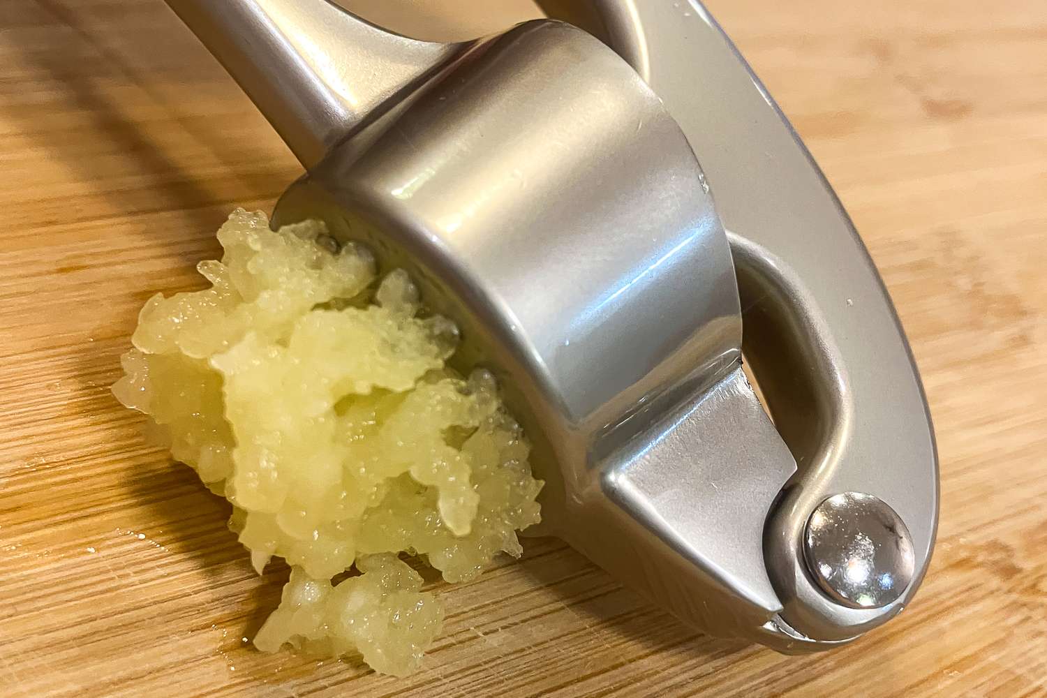 Minced garlic emerging from a garlic press on a wooden surface closeup view