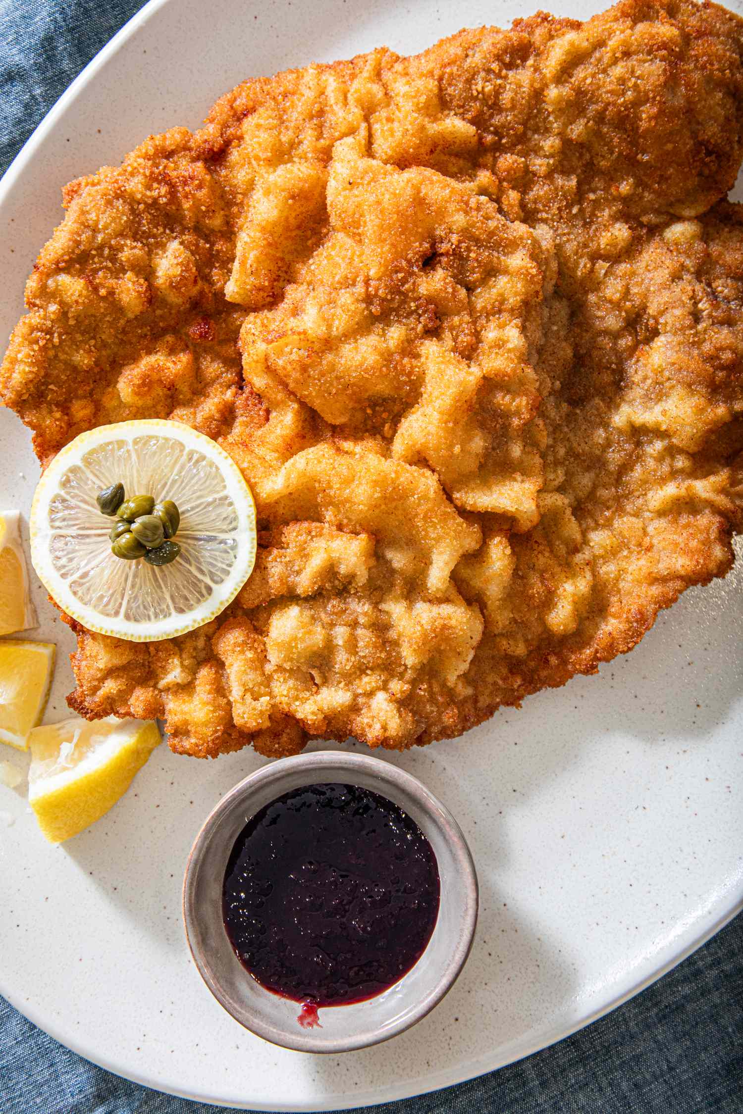 A plate of wiener schnitzel served with lemon slices and a side of berry sauce