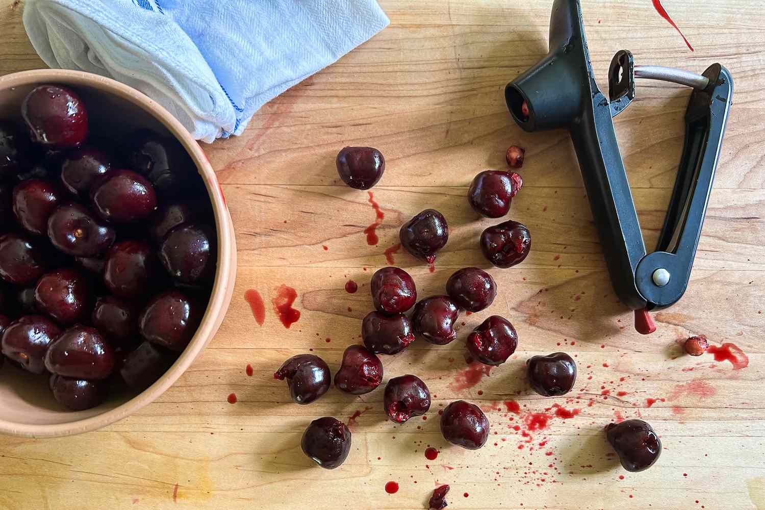 The Cuisipro cherry pitter on a wooden surface surrounded by pitted cherries