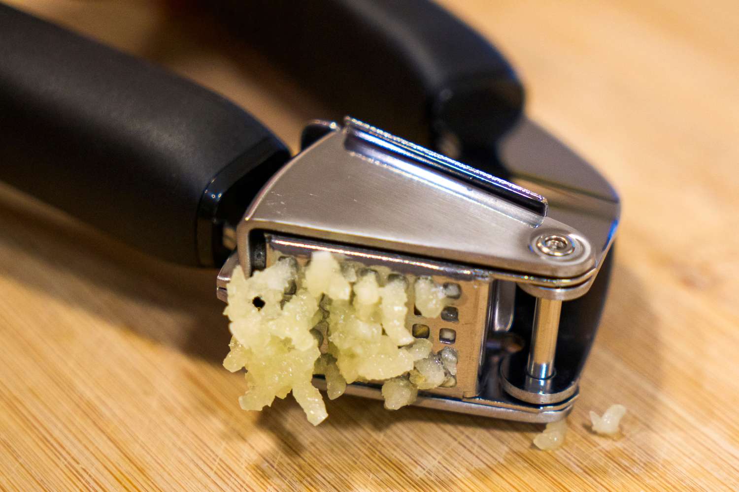A garlic press with minced garlic on a wooden surface