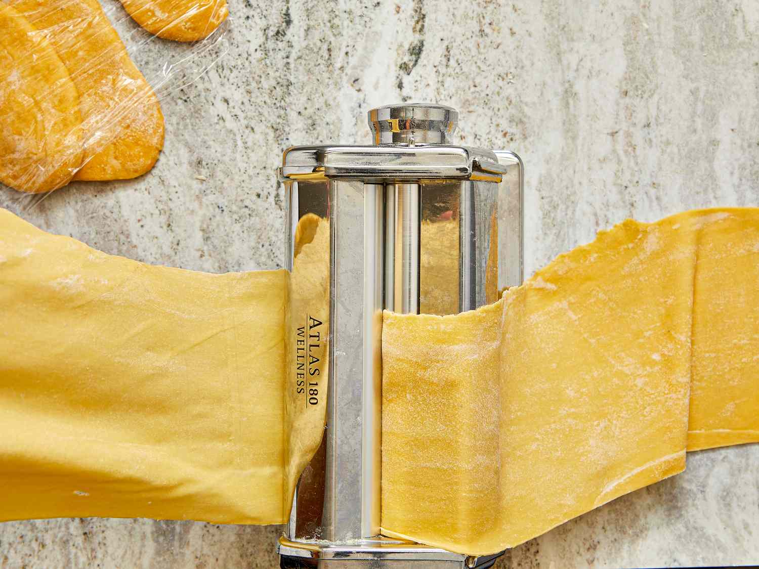 Sheet of pasta being rolled through a manual pasta machine on a countertop