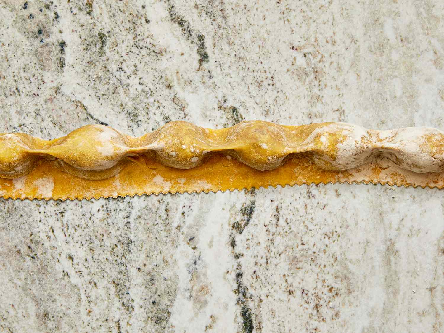 A row of agnolotti pasta on a marble surface with visible fillings