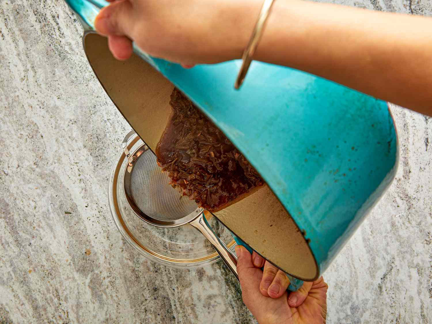 Hands pouring food from a pot into a sieve over a bowl preparation process in cooking