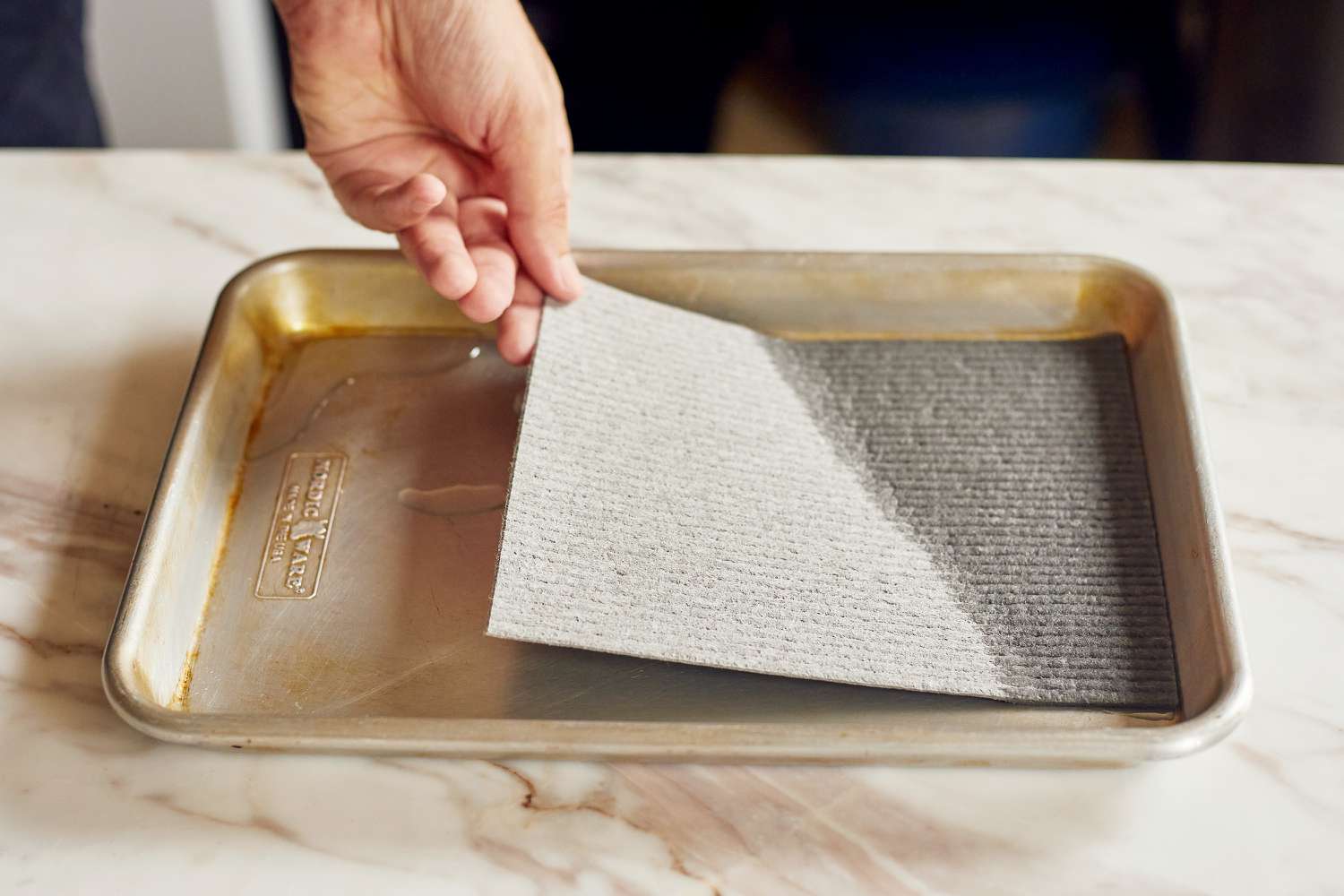 A grey Swedish dishcloth being dipped in a pan of water