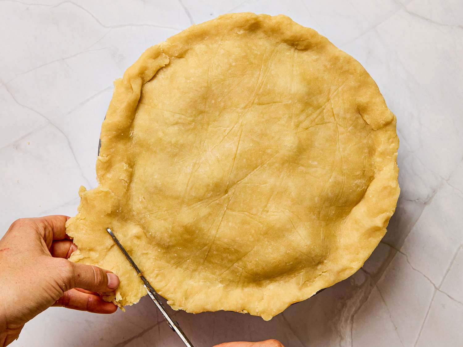 A person trimming excess pie crust with a knife