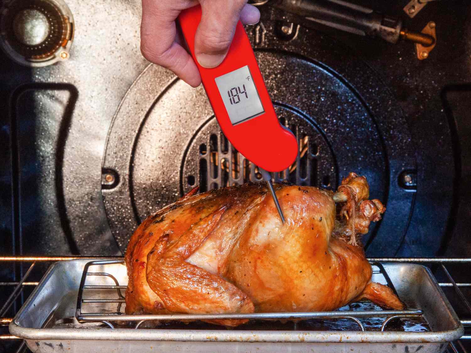 A person using a red Thermapen ONE thermometer to take the temperature of chicken.