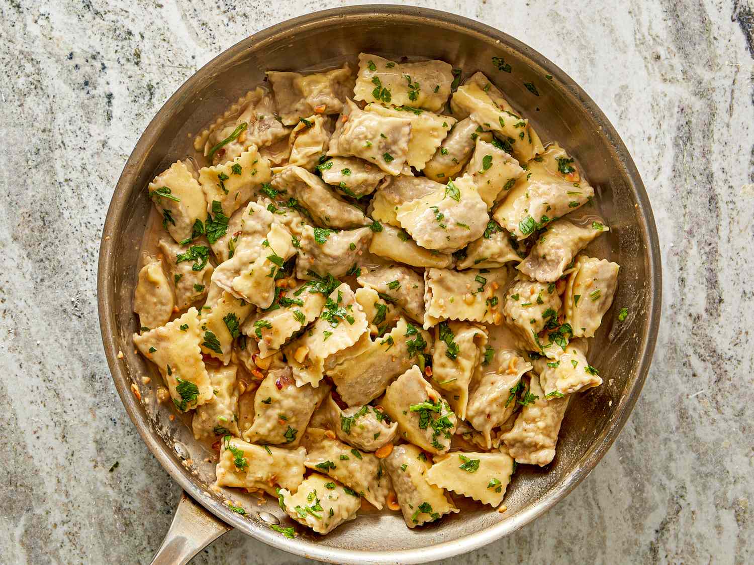 A pan of agnolotti pasta garnished with herbs on a stone countertop
