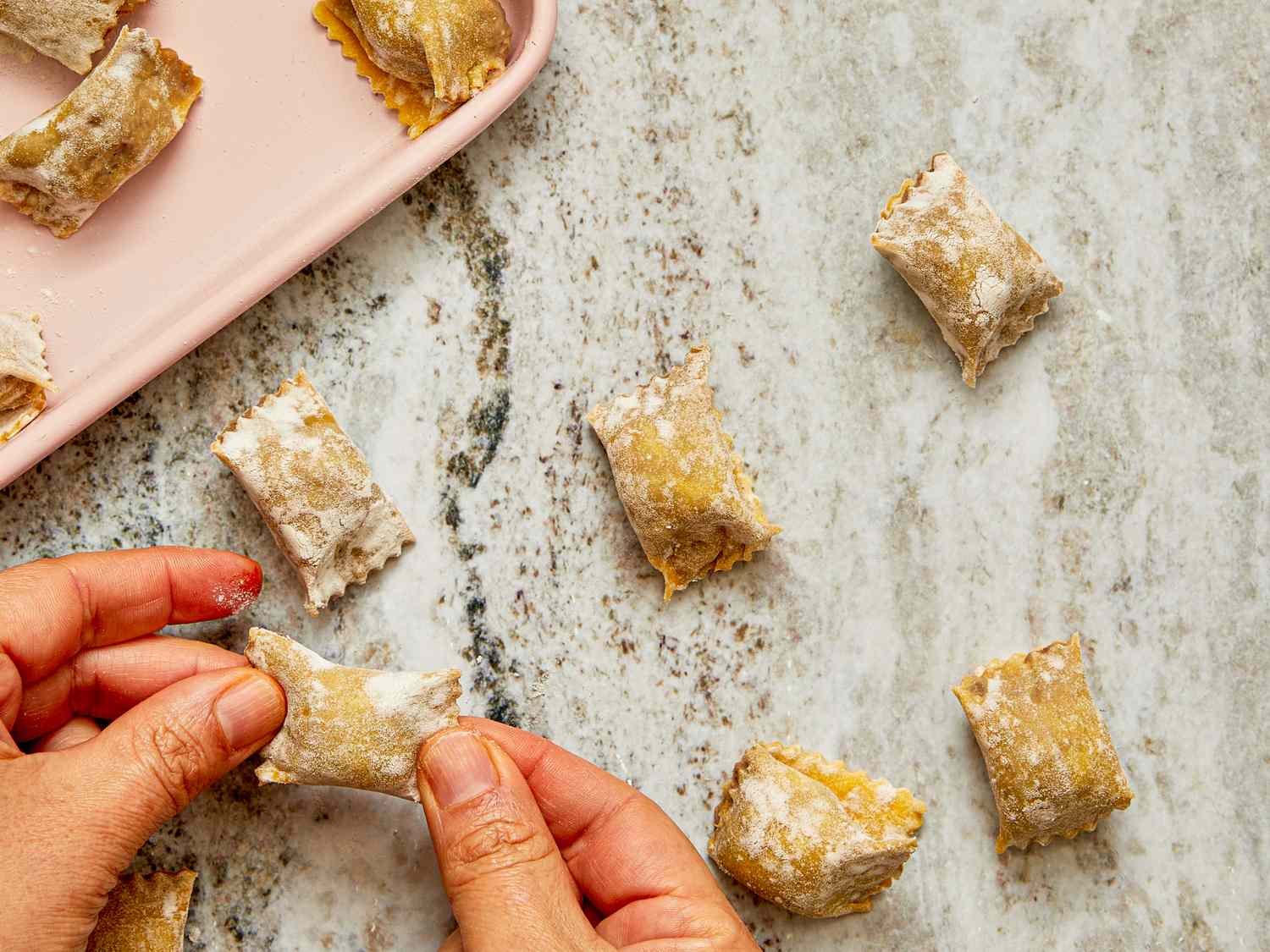 Hands shaping small pieces of pasta filled with a filling on a countertop demonstrating a culinary preparation process