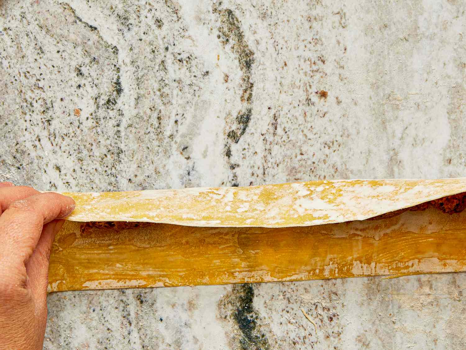 Hand lifting a sheet of filled pasta to show its layered structure