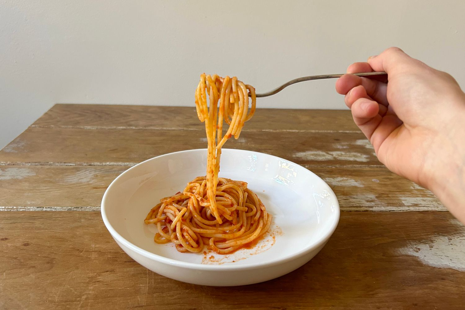 A hand twirling a forkful of spaghetti in a white glazed pasta bowl