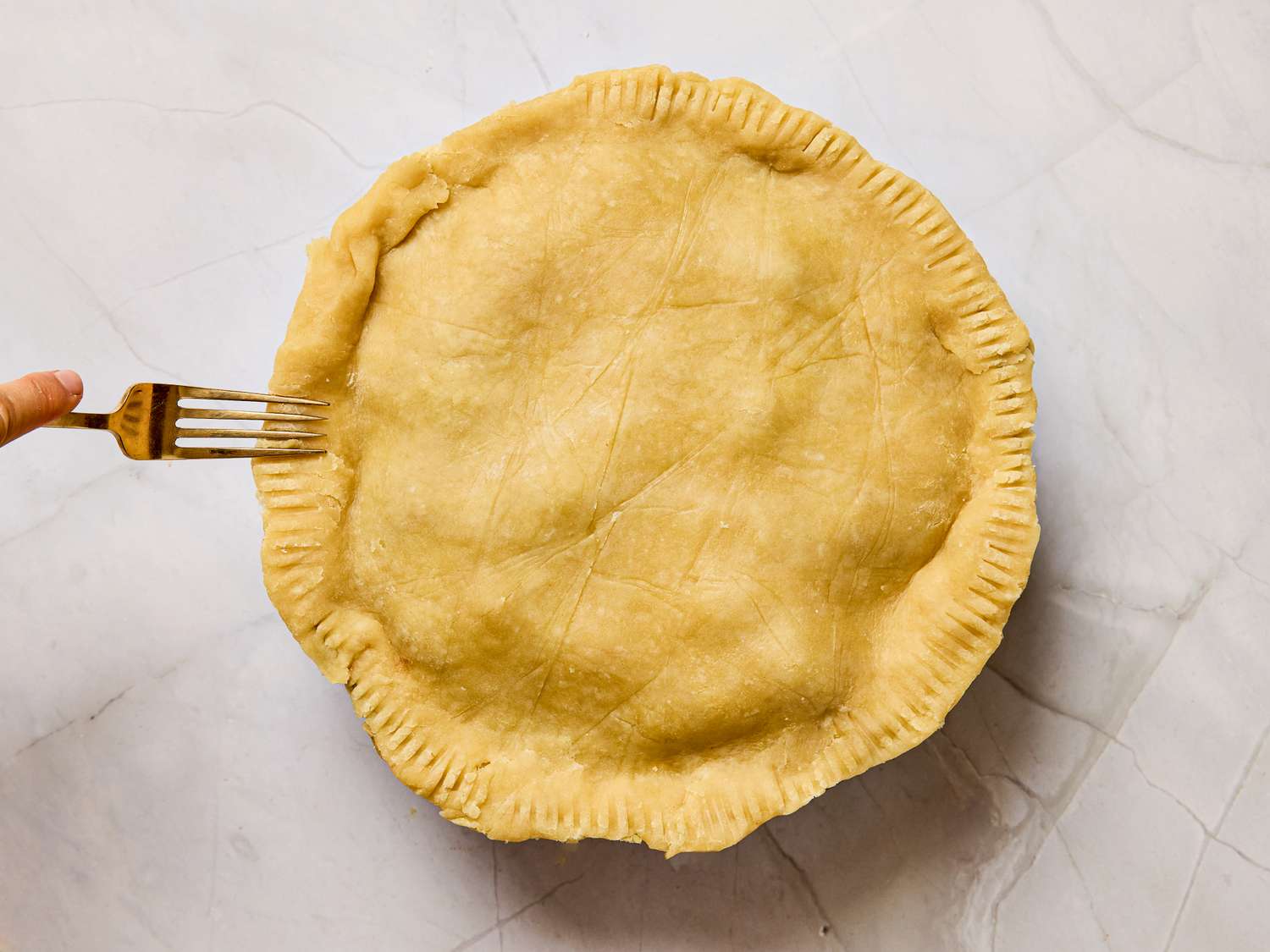 Person using a fork to crimp the edges of a pie crust before baking